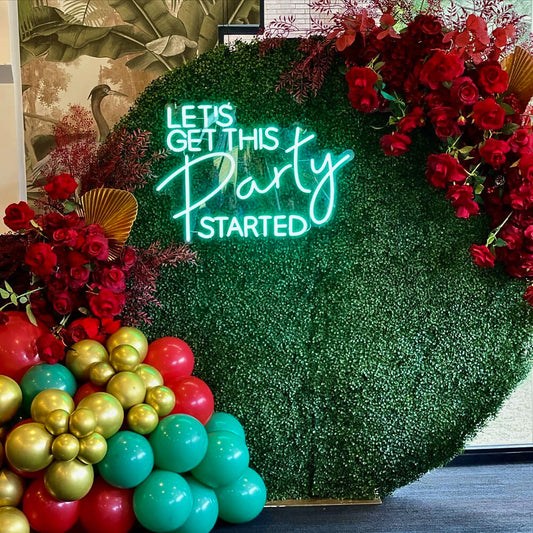 green lets get this party started neon sign hanging on garden wall backdrop with flowers and balloons