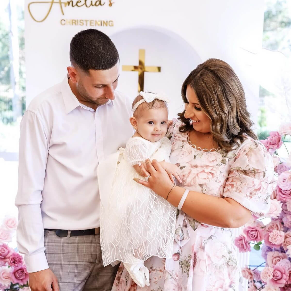 man and woman holding baby with pink floral and white backdrop background