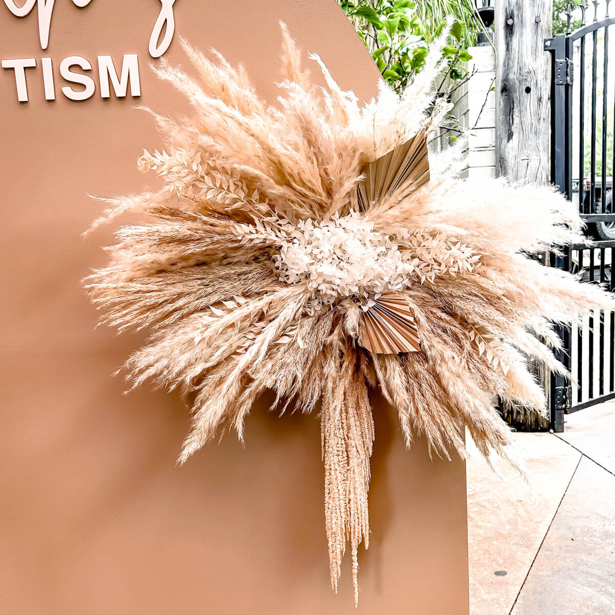 boho flower arrangement attached to beige backdrop with pampas, palm leaves and hanging amaranthus