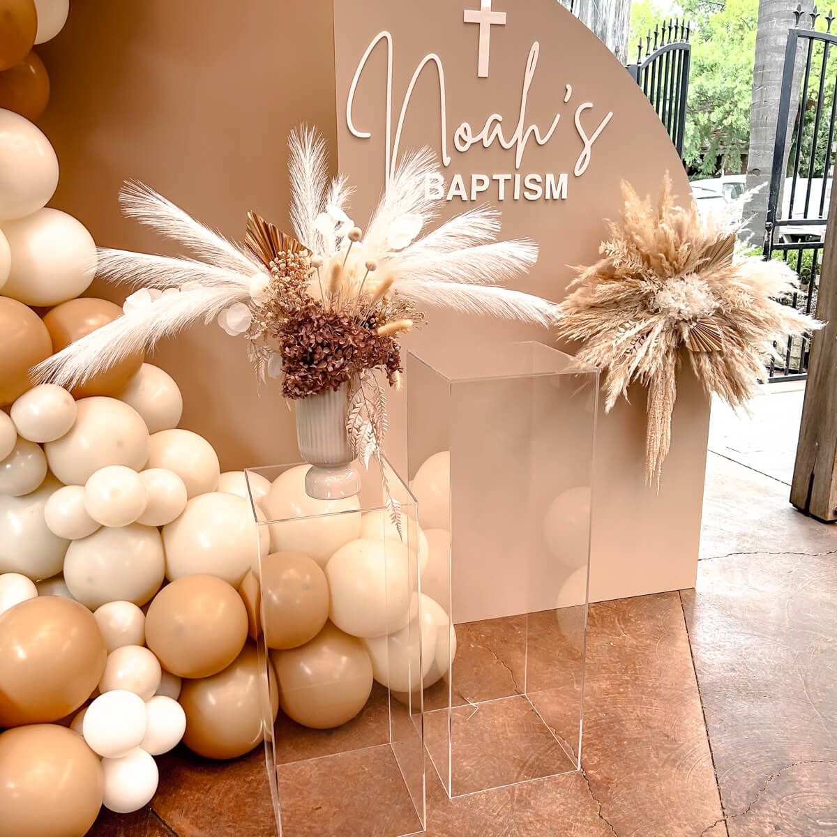 boho flower arrangement placed on top of clear plinths in front of beige backdrops at baptism event