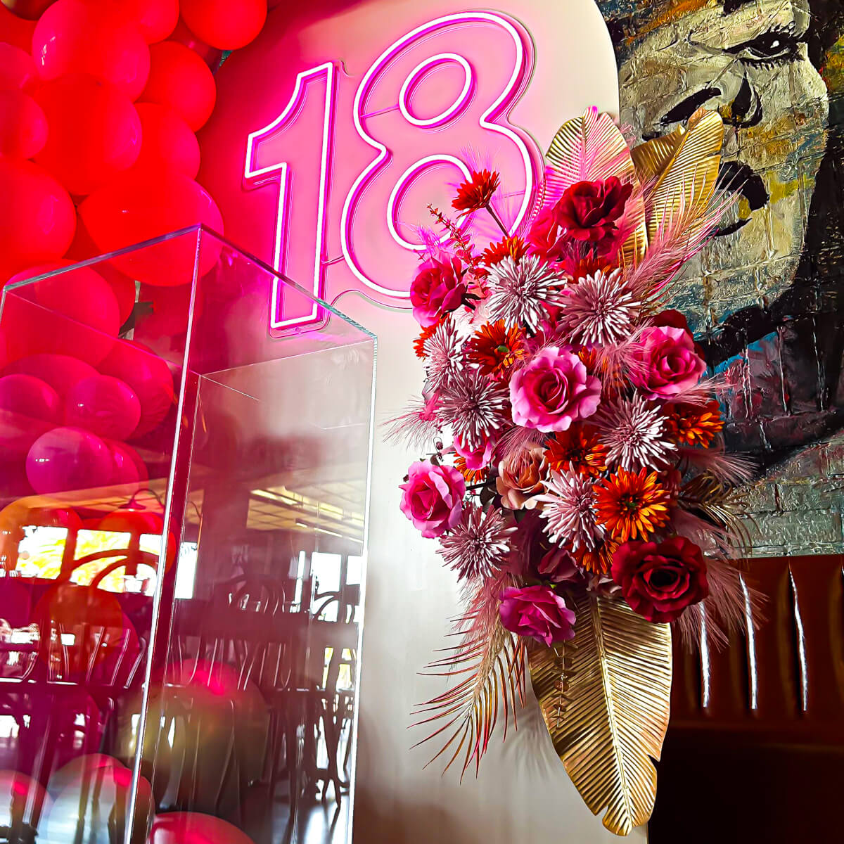 pink, orange and red flower arrangement with gold palm leaves hanging on arch backdrop with 18 neon sign