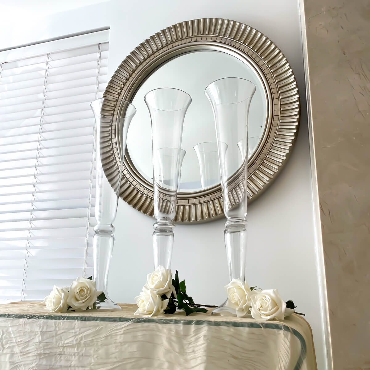 three tall wedding glass vases placed on glass table with white roses and mirror on wall