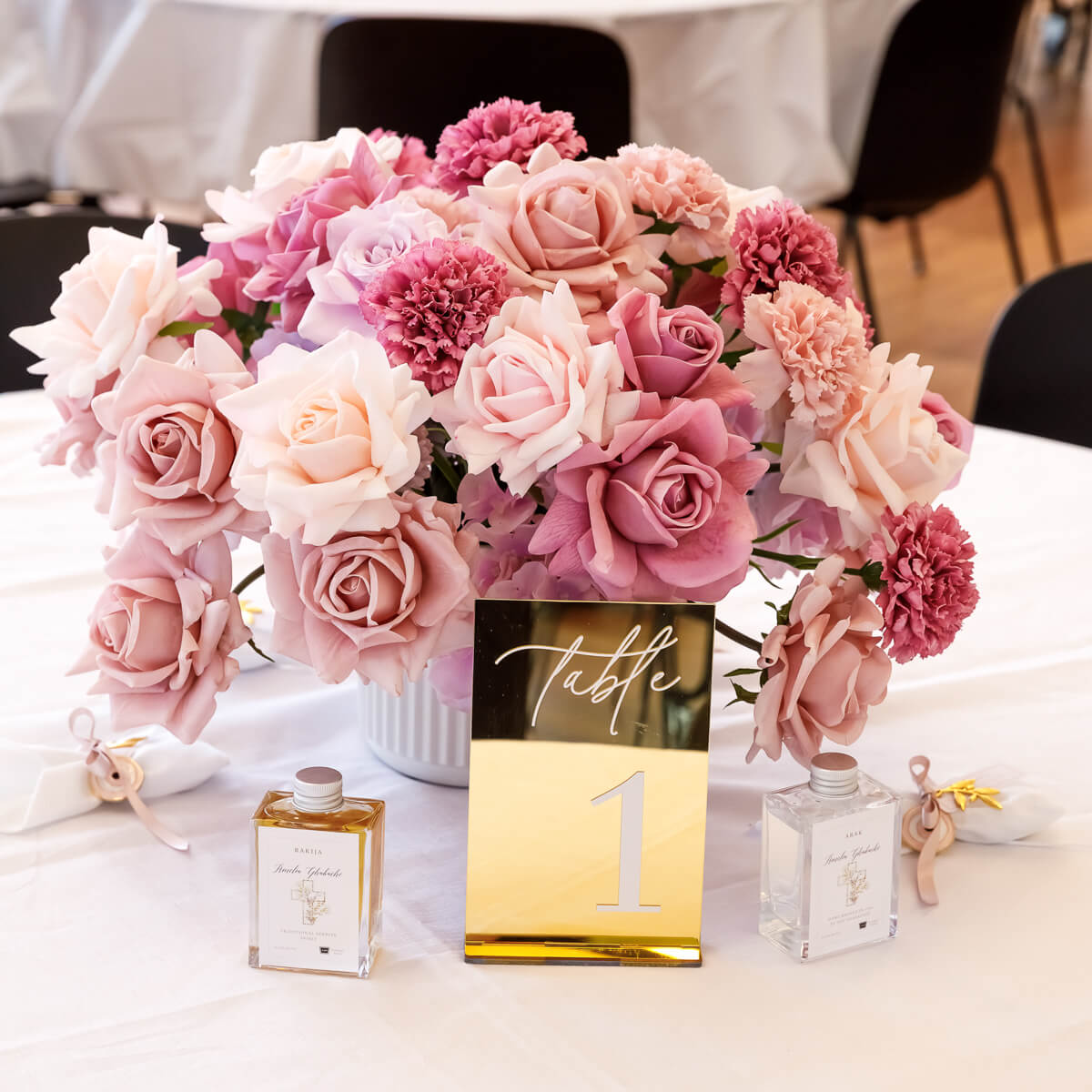 mixed pink and lilac flower arrangement in white vase next to gold table number