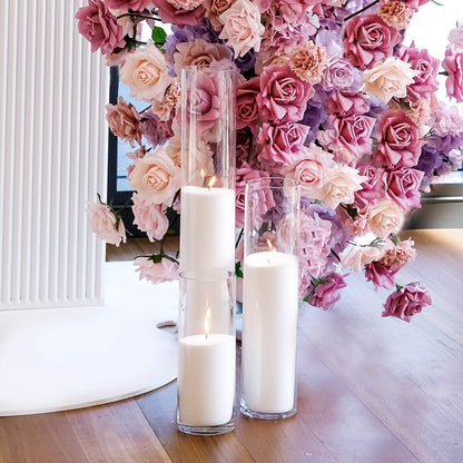 three white sand candles on floor in front of mixed pink and purple flower arrangement