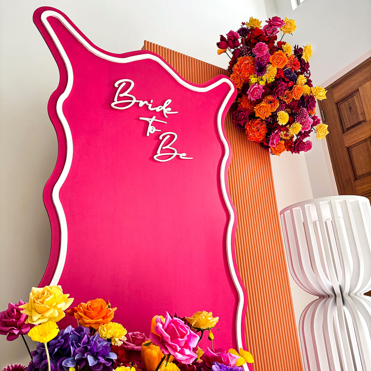 hot pink and burnt orange backdrop with bright floral arrangements and white plinth