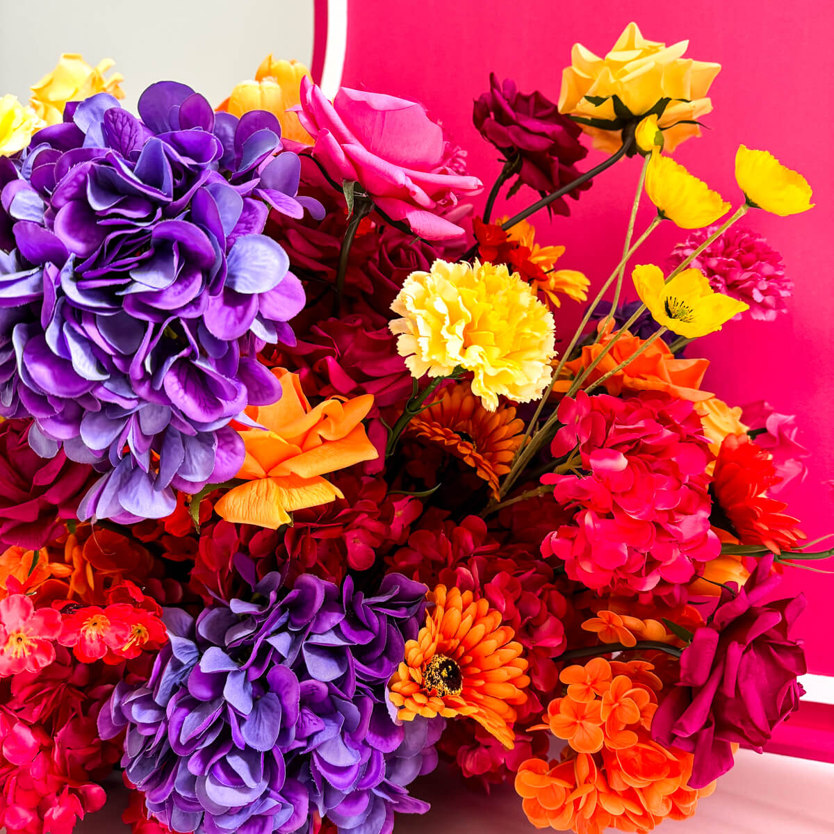 Close up of purple hydrangeas and yelow roses on floor in front of hot pink backdrop