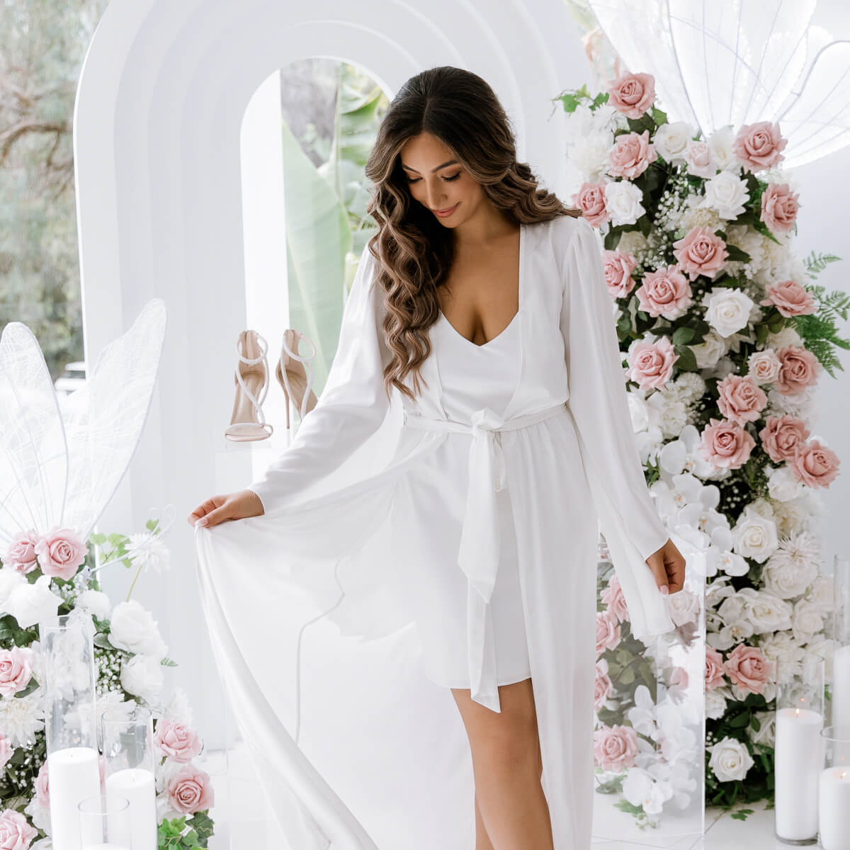 bride standing in front of white 3d arch backdrop and pink flower arrangements on wedding day