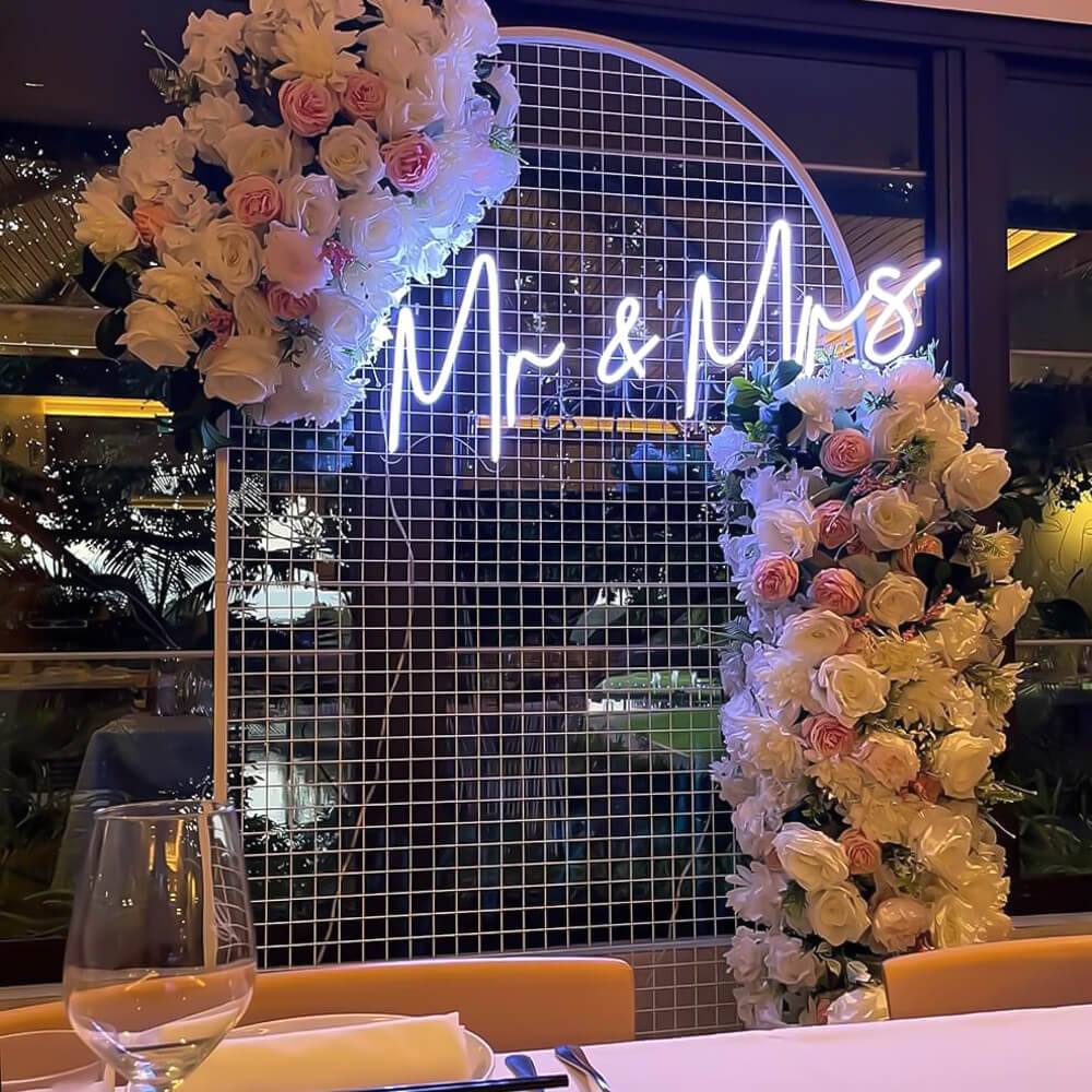 white arch mesh backdrop with neon sign and white flower arrangement at wedding