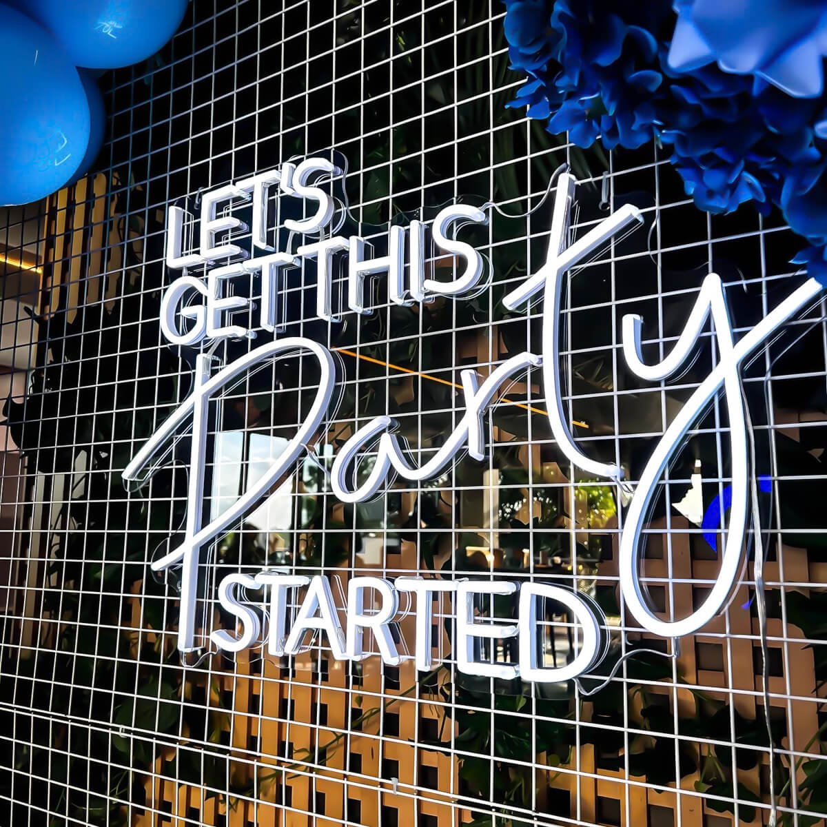 white let's get this party started neon sign hanging on white mesh backdrop with blue flowers and balloons