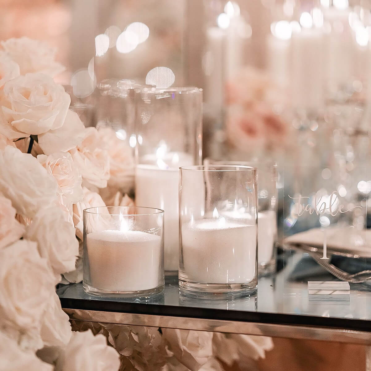 white sand candles on glass table next to white roses