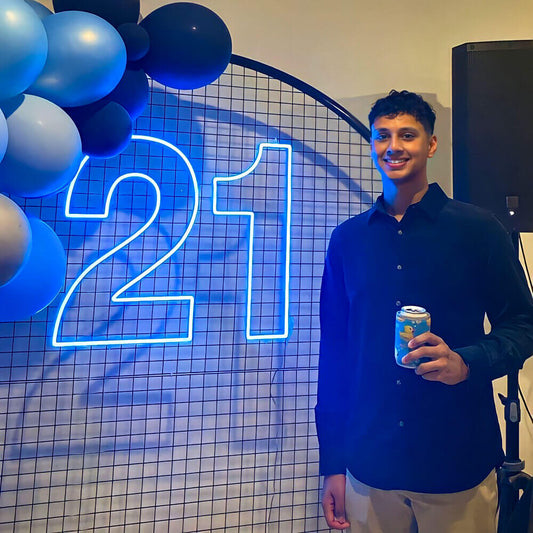 boy standing in front of blue 21 neon sign on backdrop frame with balloon garland