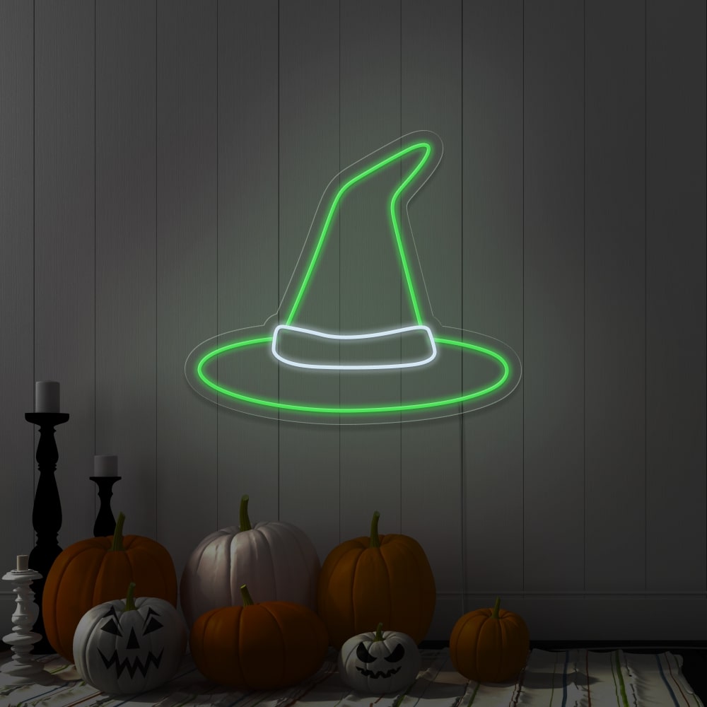 green witch hat neon sign hanging on wall above pumpkins