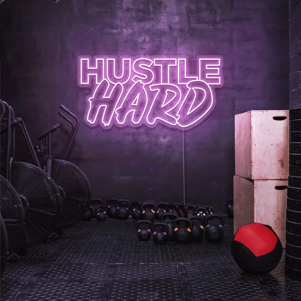 light pink hustle hard neon sign hanging on gym wall