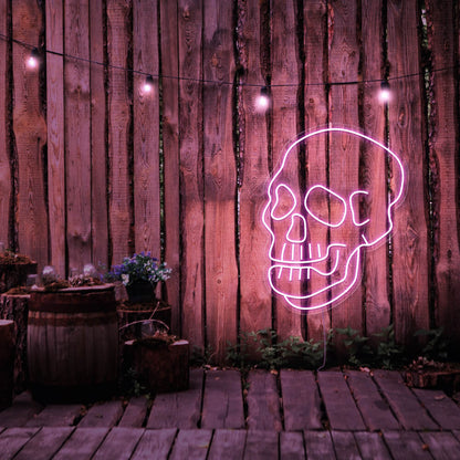 light pink skull neon sign hanging on timber fence