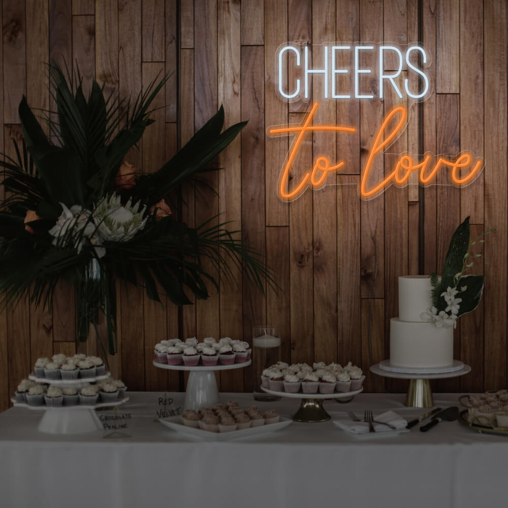 orange cheers to love neon sign hanging above dessert table