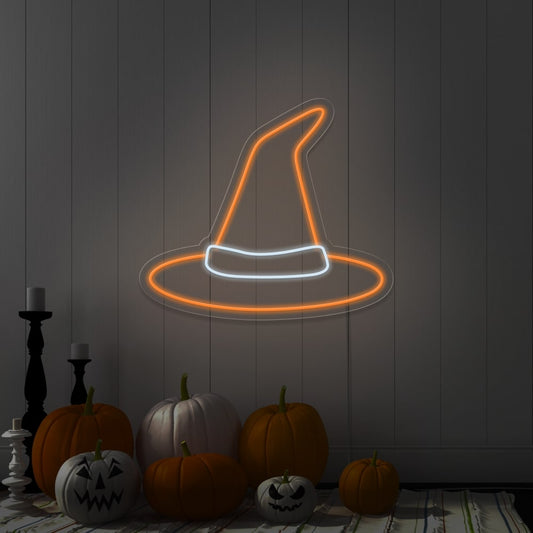 orange witch hat neon sign hanging on wall above pumpkins