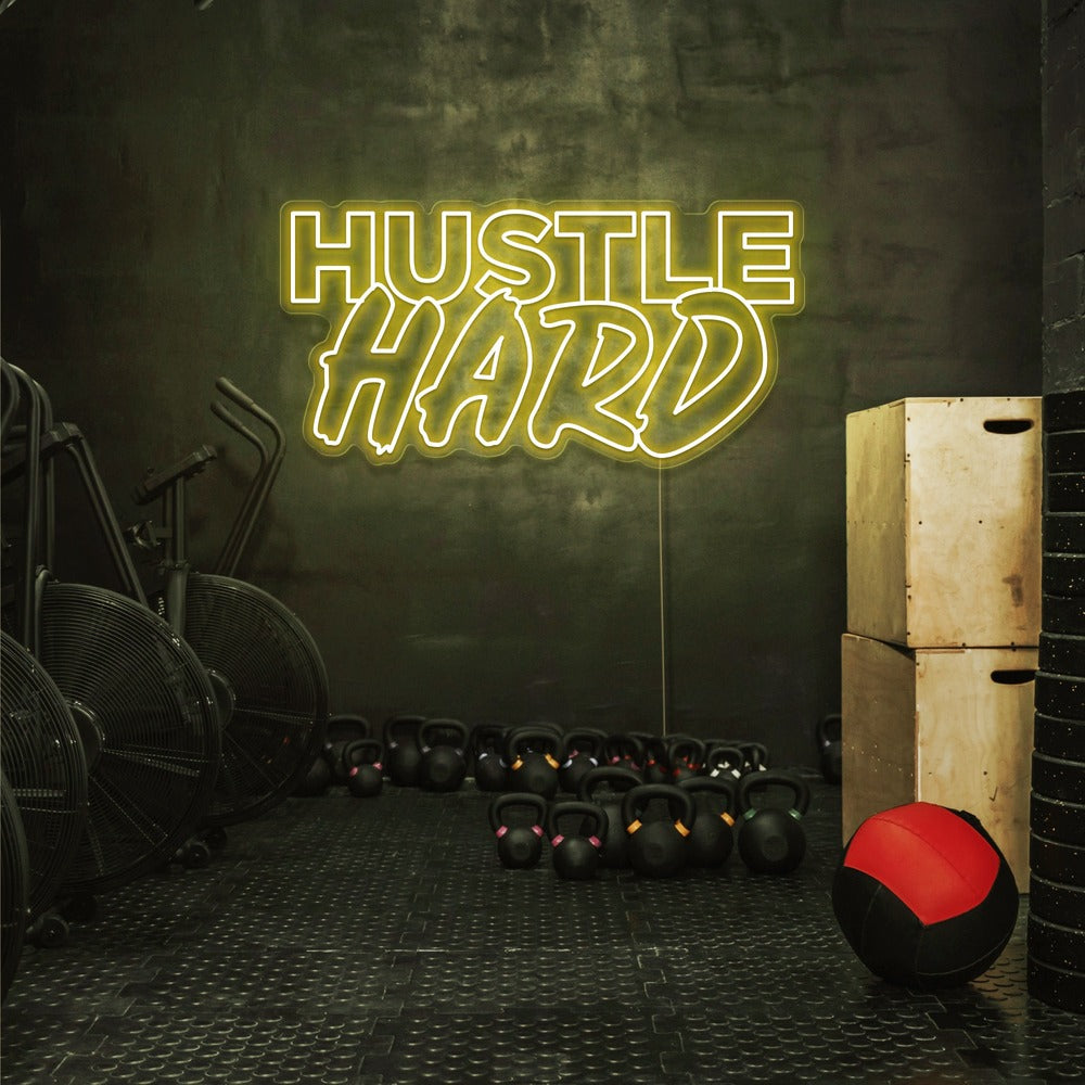 yellow hustle hard neon sign hanging on gym wall